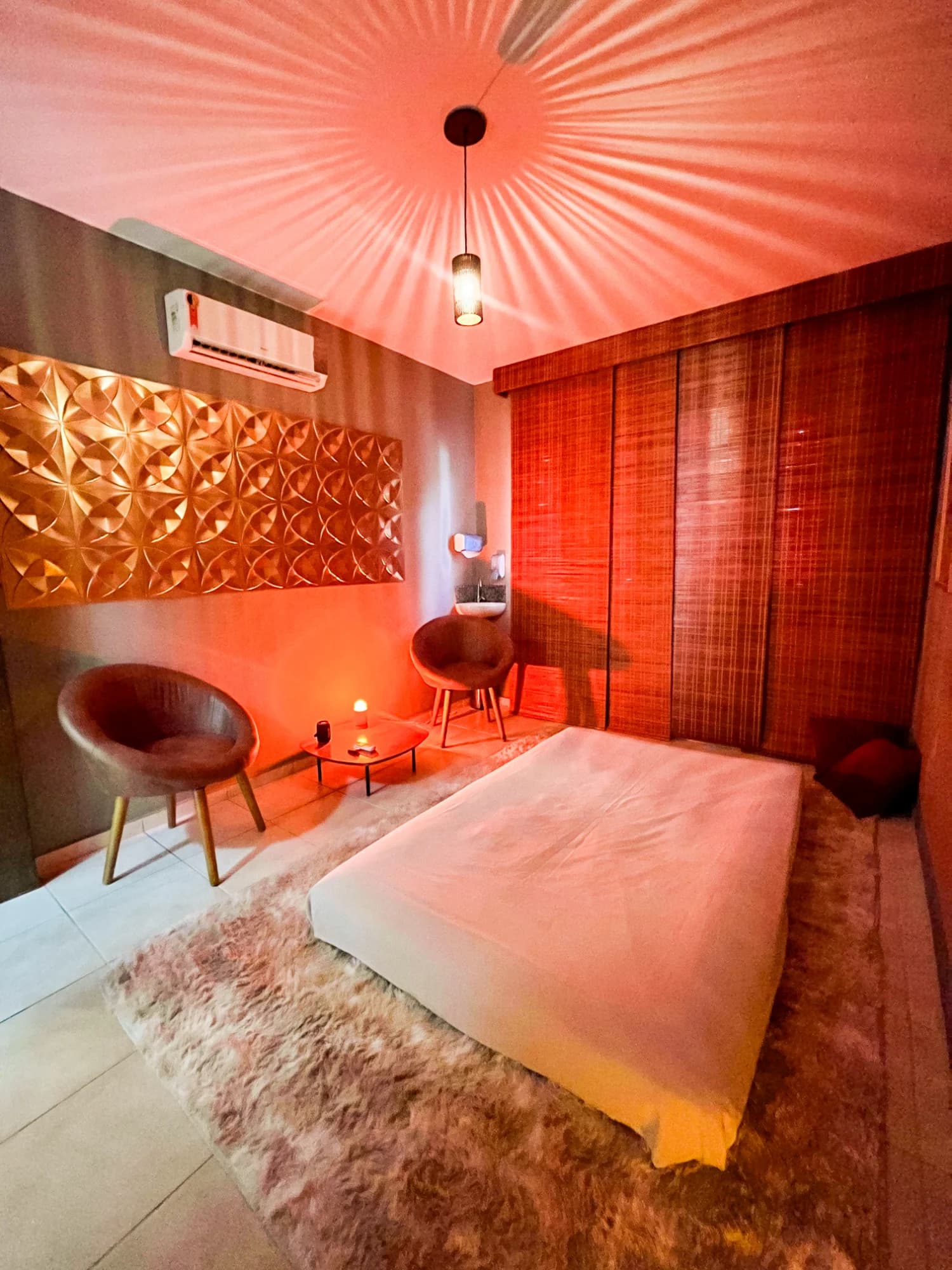 Sala Sândalo do Espaço Cor em luz quente, com futon, tapete felpudo e painel dourado